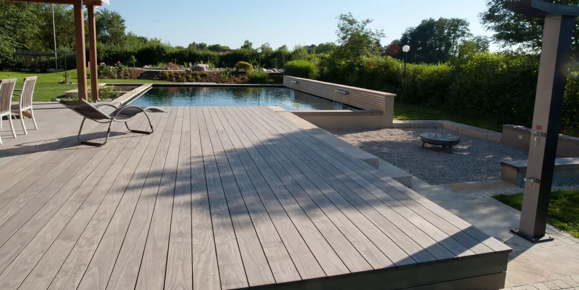 Grande terrasse de jardin en Accoya autour d’un bassin naturel, coin feu en gravier